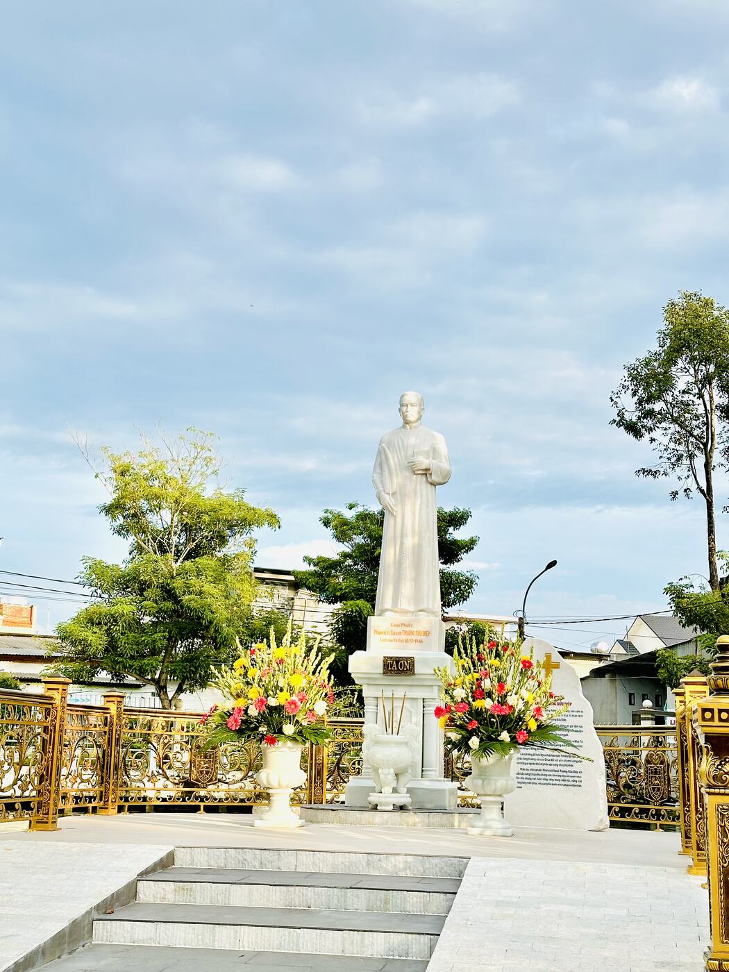 Tượng đài Chân phước giữa hai bình hoa tươi trong buổi sáng ngày lễ
